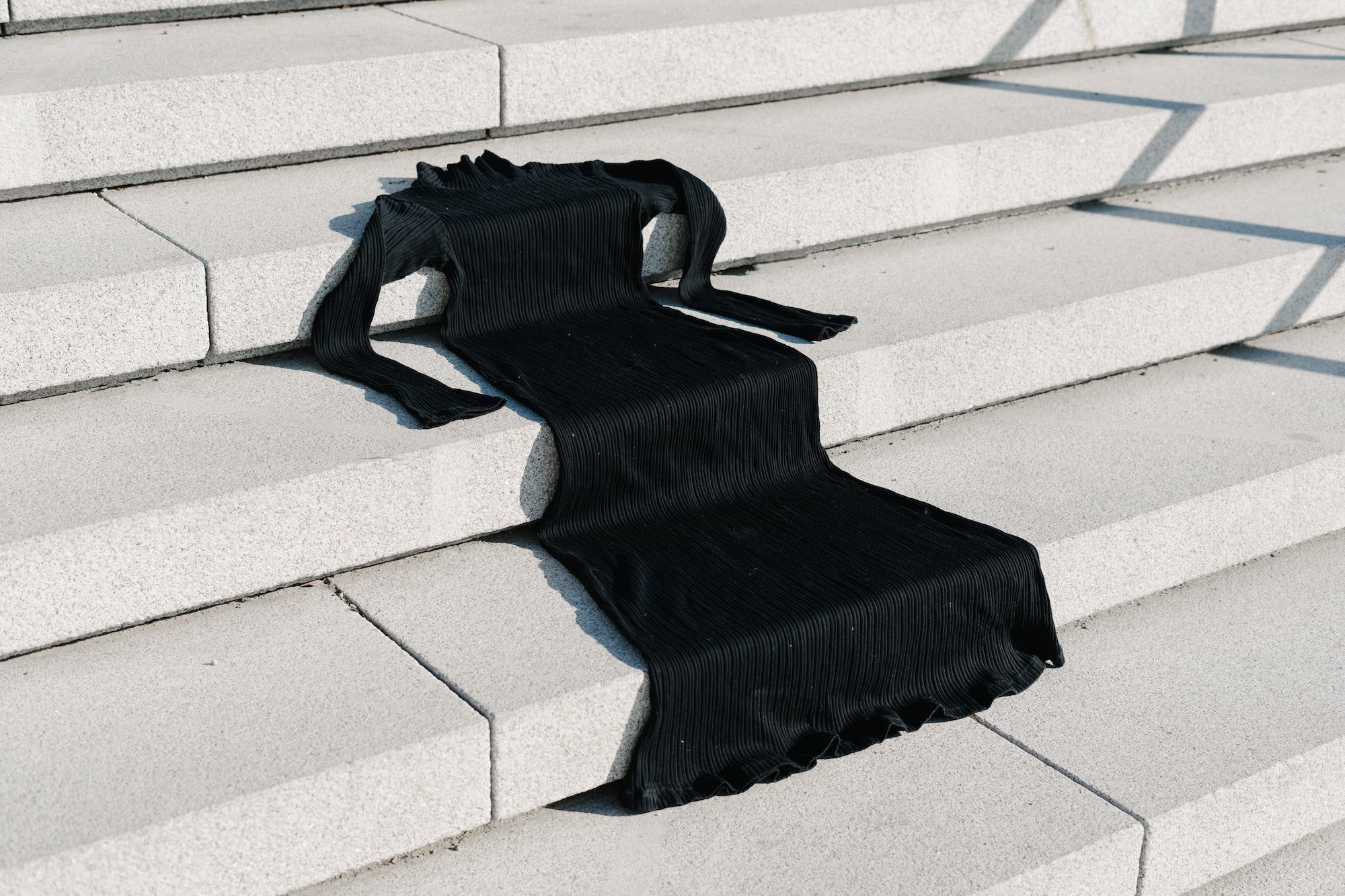 Black turtleneck long‑sleeve dress draped across light gray concrete stairs.
